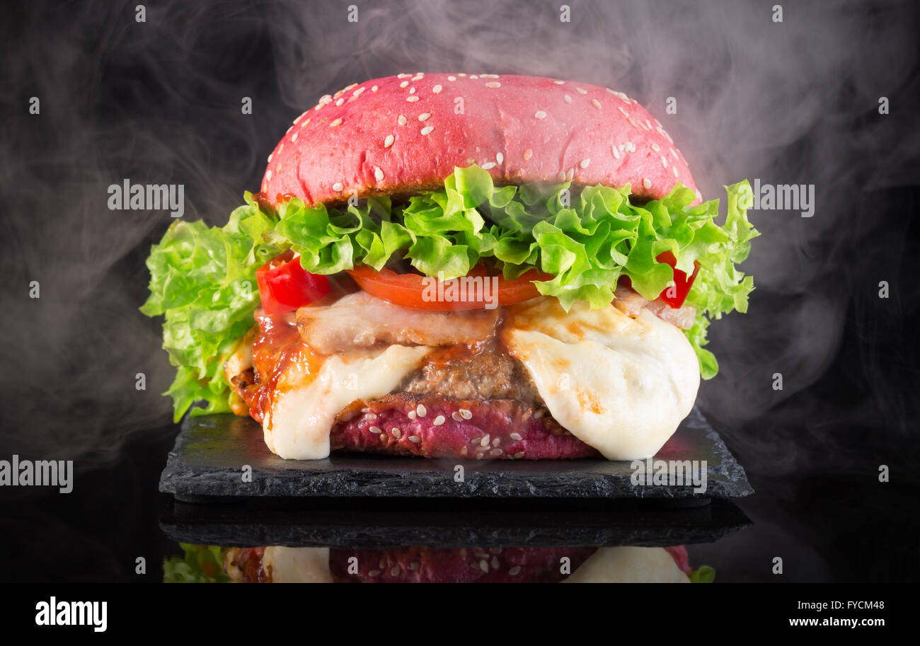 große rote Hamburger mit Rauch auf Schiefer Tisch. Stockfoto