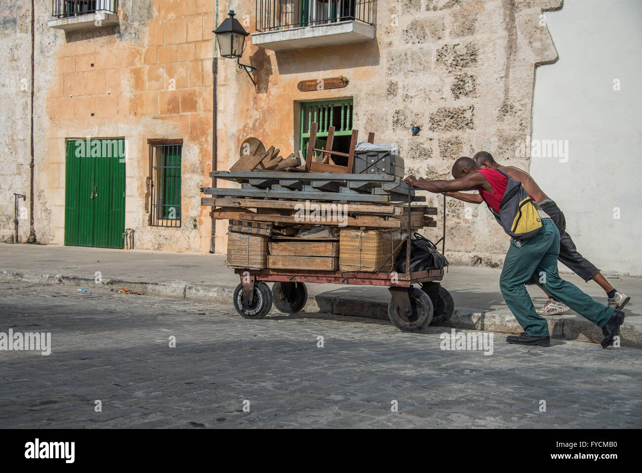 2 kubanische Männer schieben einen Wagen beladen mit Elemente bergauf in Alt-Havanna, Kuba Stockfoto
