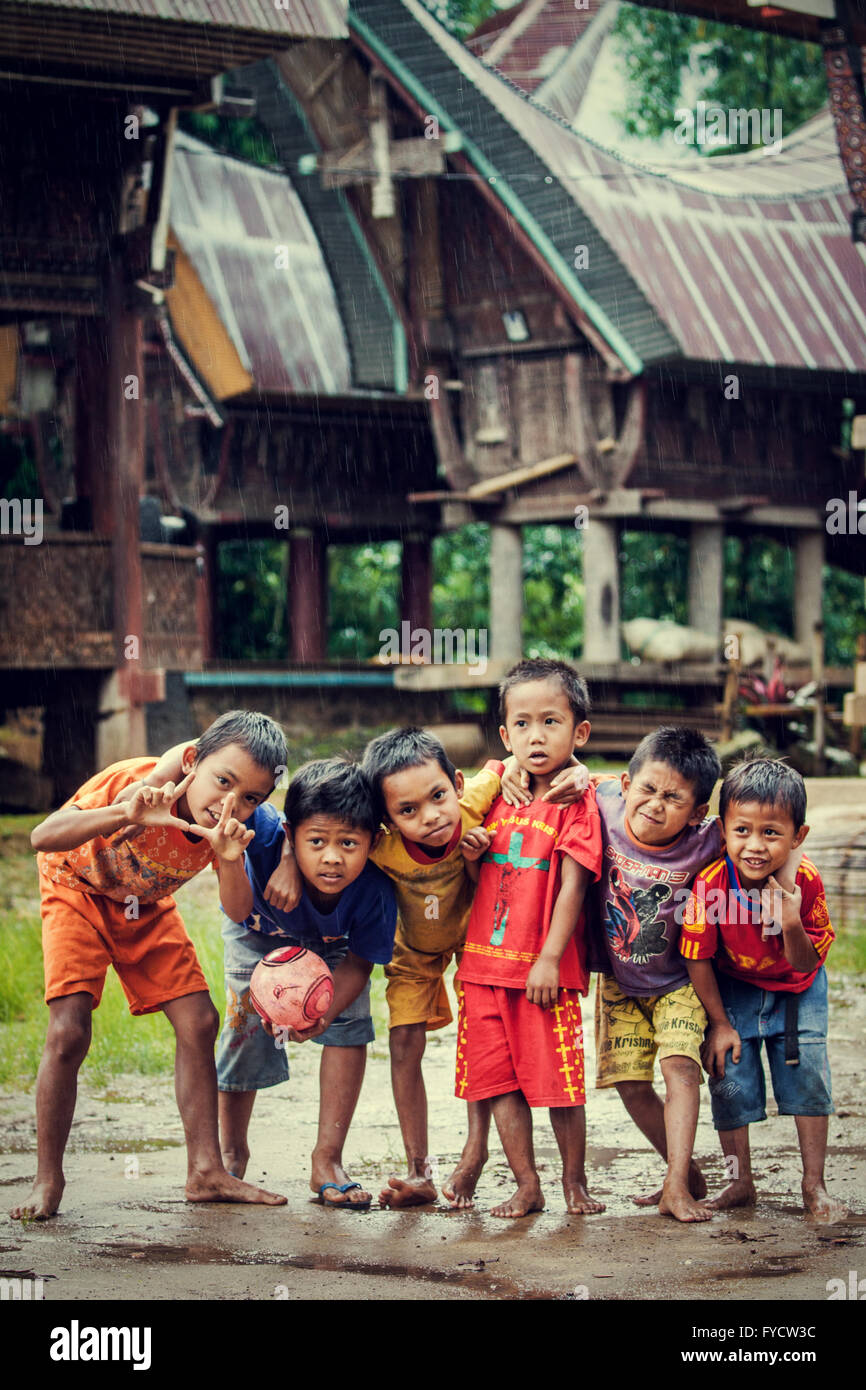Traditionelle Torajan Tongkonan Häuser mit einer Bande von jungen einheimischen Kinder posieren für ein offenherziger Foto Stockfoto