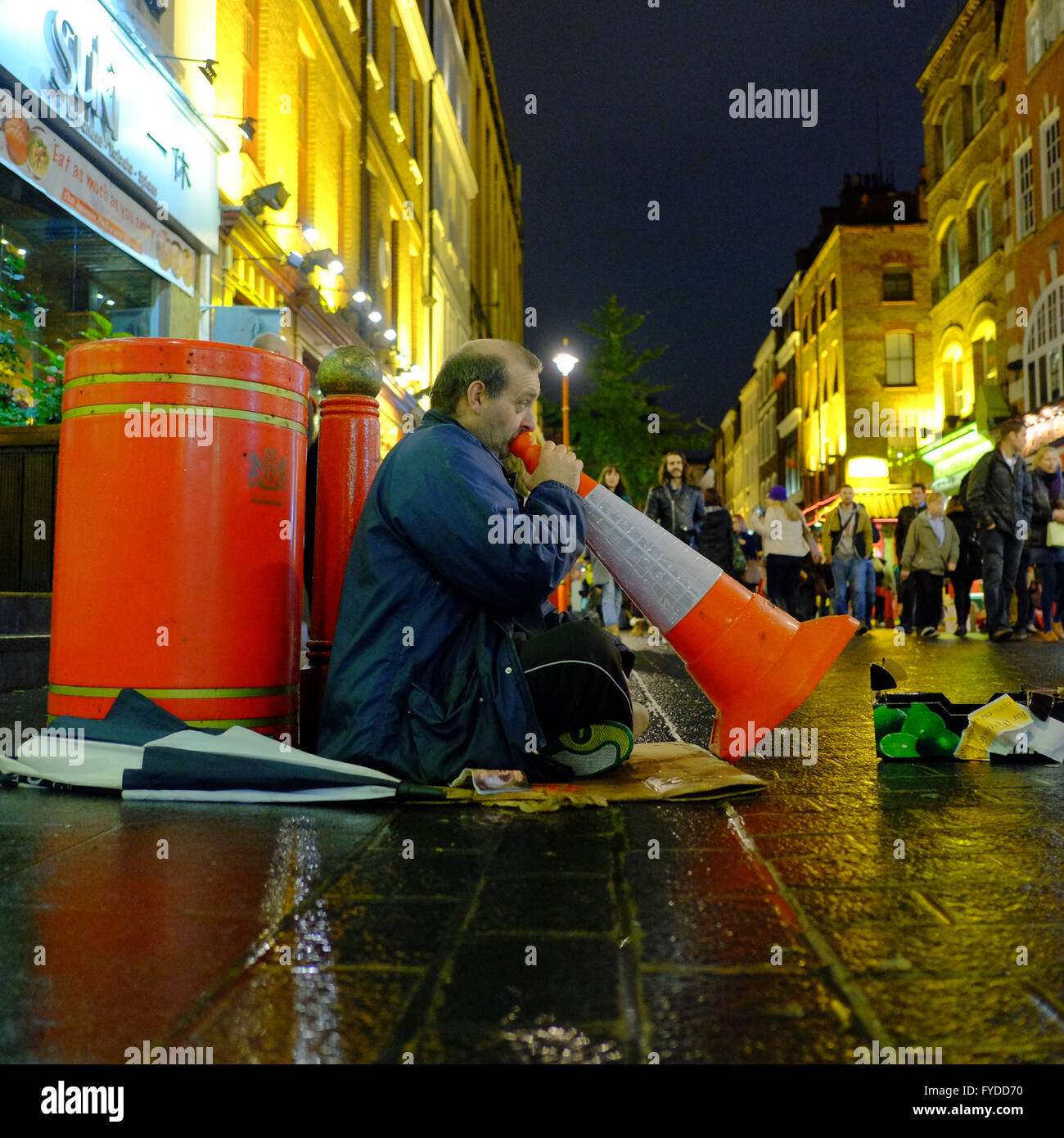 Mann sitzt auf dem Bürgersteig Musizieren durch Einblasen auf einem Kegel Verkehr in London Stockfoto