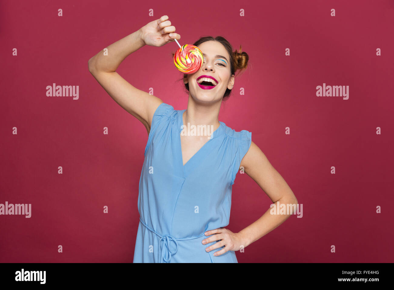 Glücklich erregte junge Frau überdeckt rosa Hintergrund ihr Auge mit bunten Lollipop. Stockfoto