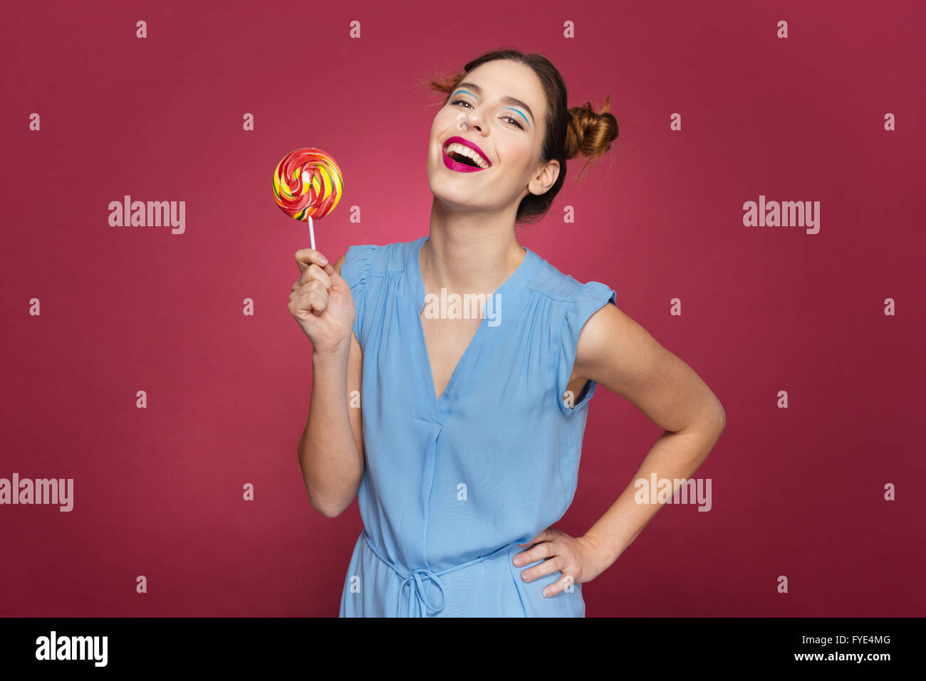 Fröhliche hübsche junge Frau halten bunte Lutscher und lachen über rosa Hintergrund Stockfoto