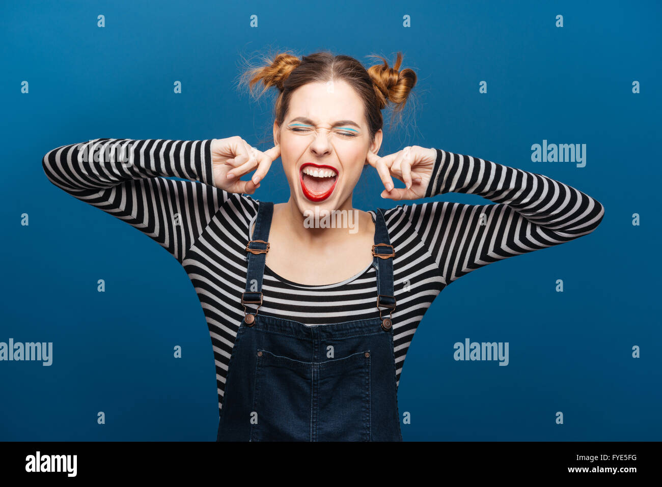Lustige böse junge Frau mit geschlossenen Ohren Augen bu Finger überdeckt blauem Hintergrund Stockfoto