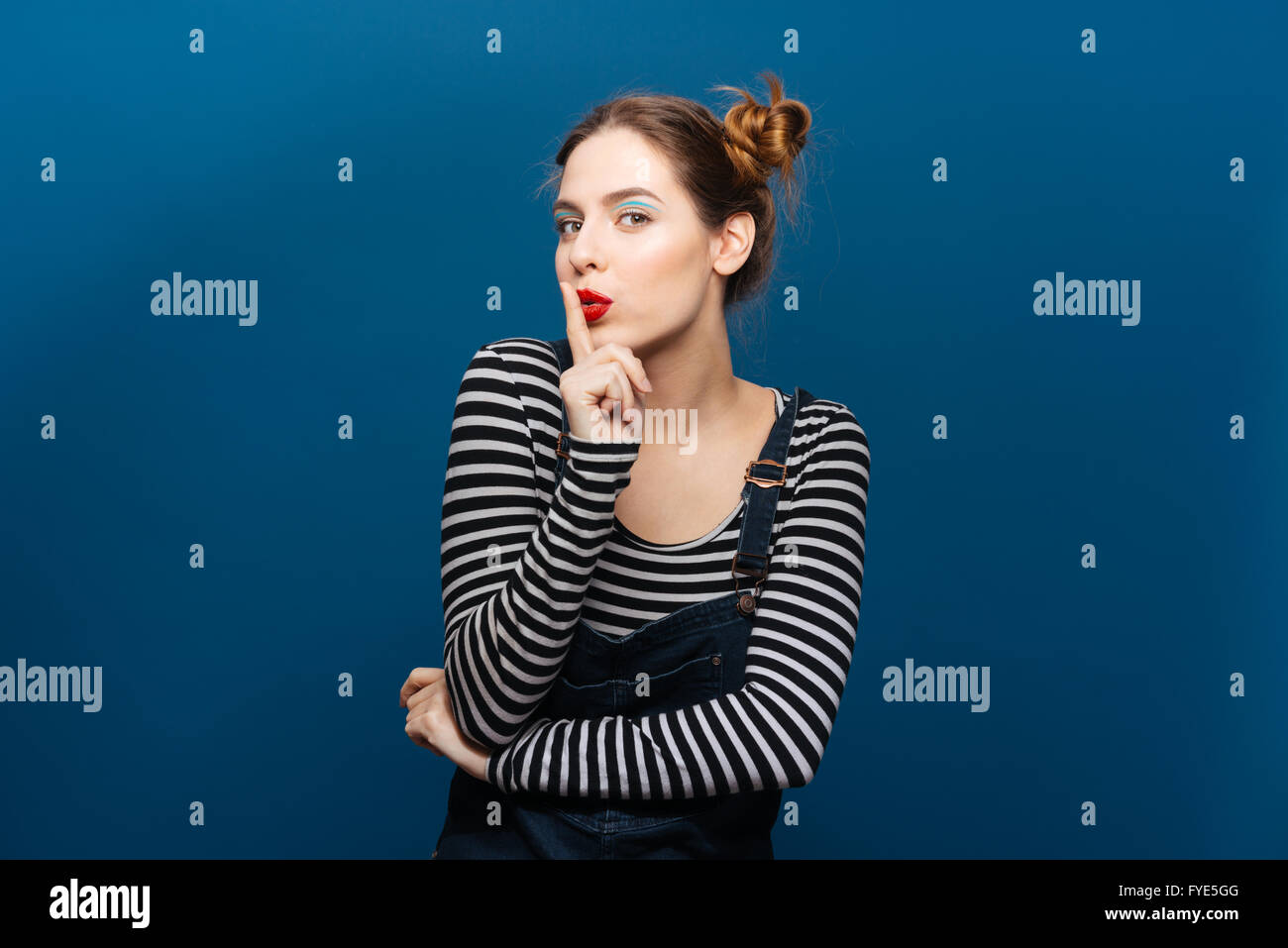 Unterhaltsame attraktive junge Frau zeigt stille Geste auf blauem Hintergrund Stockfoto