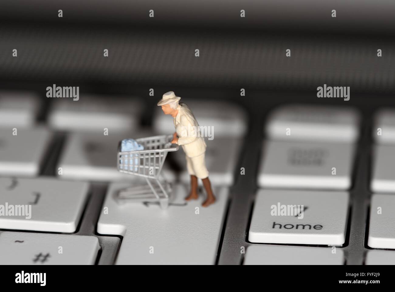 Eine ältere Frau, die einen Supermarkt Einkaufswagen über eine Laptoptastatur drücken Stockfoto