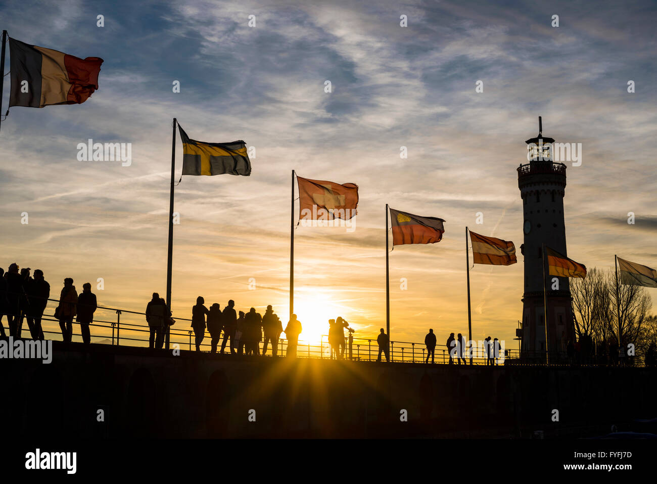 Silhouetten von Menschen und Flaggen bei Sonnenuntergang, Hafen in Lindau am Bodensee, Bayern, Deutschland Stockfoto