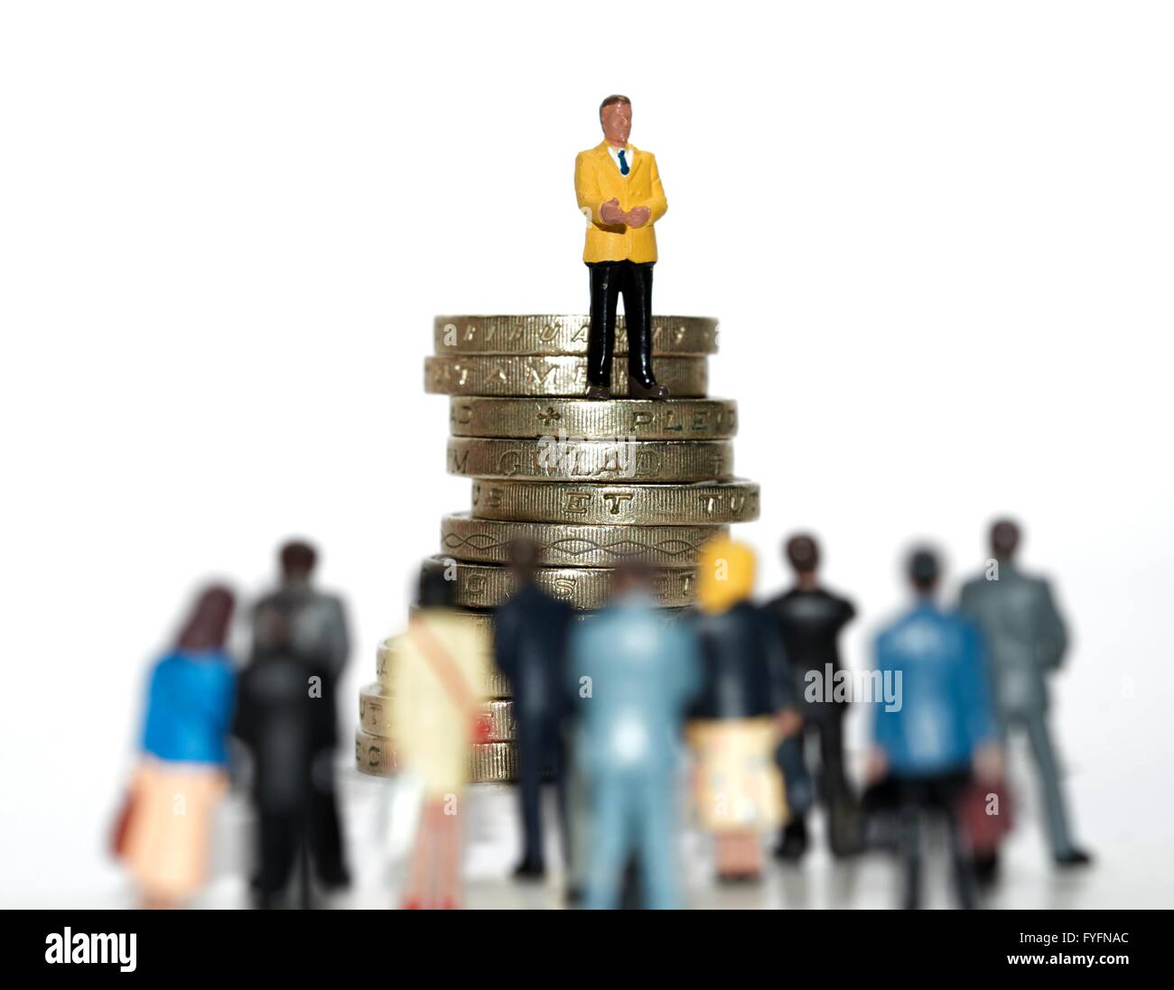 Beratung Konzept Geld. Ein Miniatur-Geschäftsmann stand am Anfang von einem Stapel von 1 Pfund-Münzen im Gespräch mit einer Menge von Menschen Stockfoto