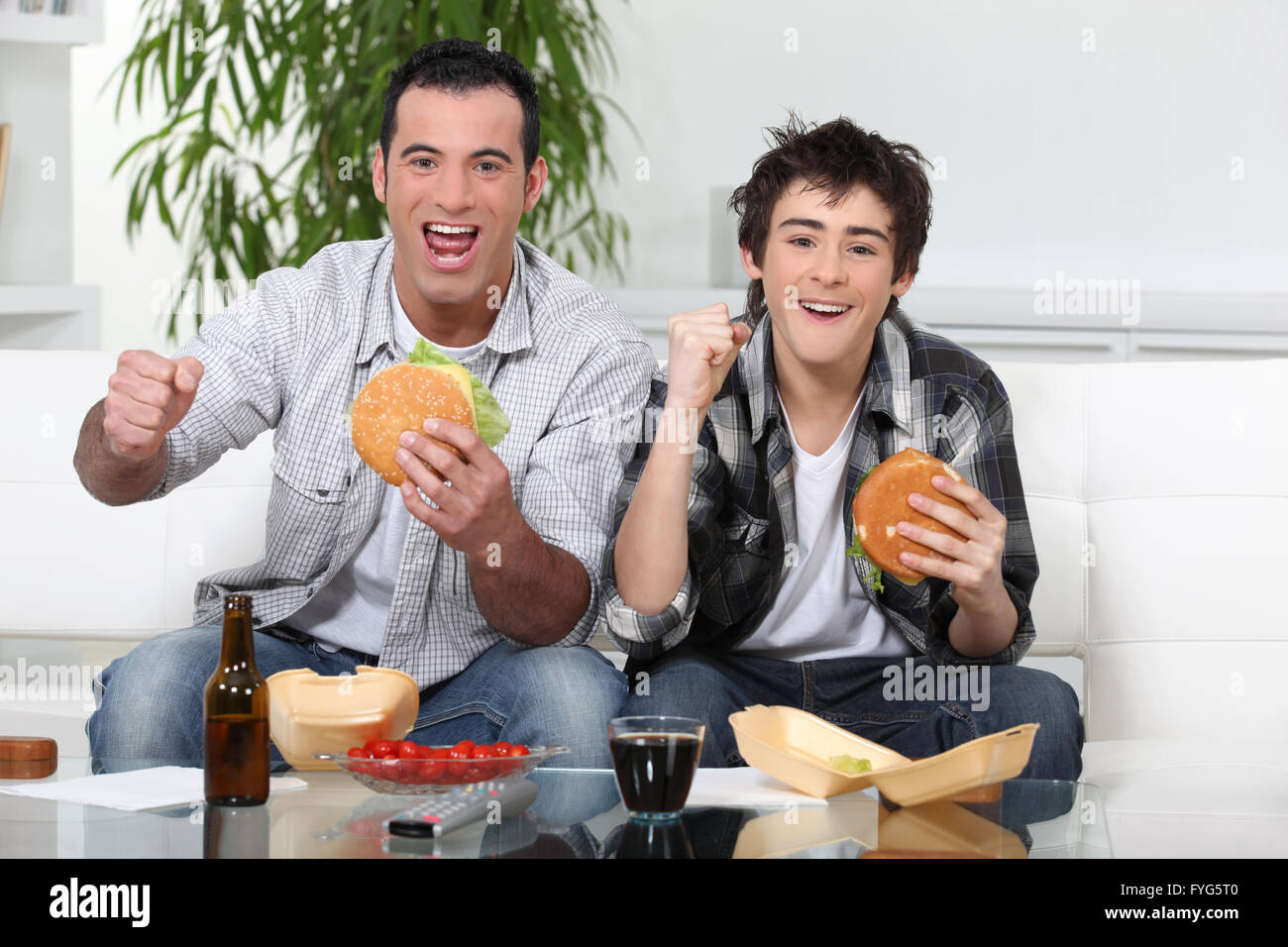 Vater und Sohn essen Burger vor Fernseher Stockfoto