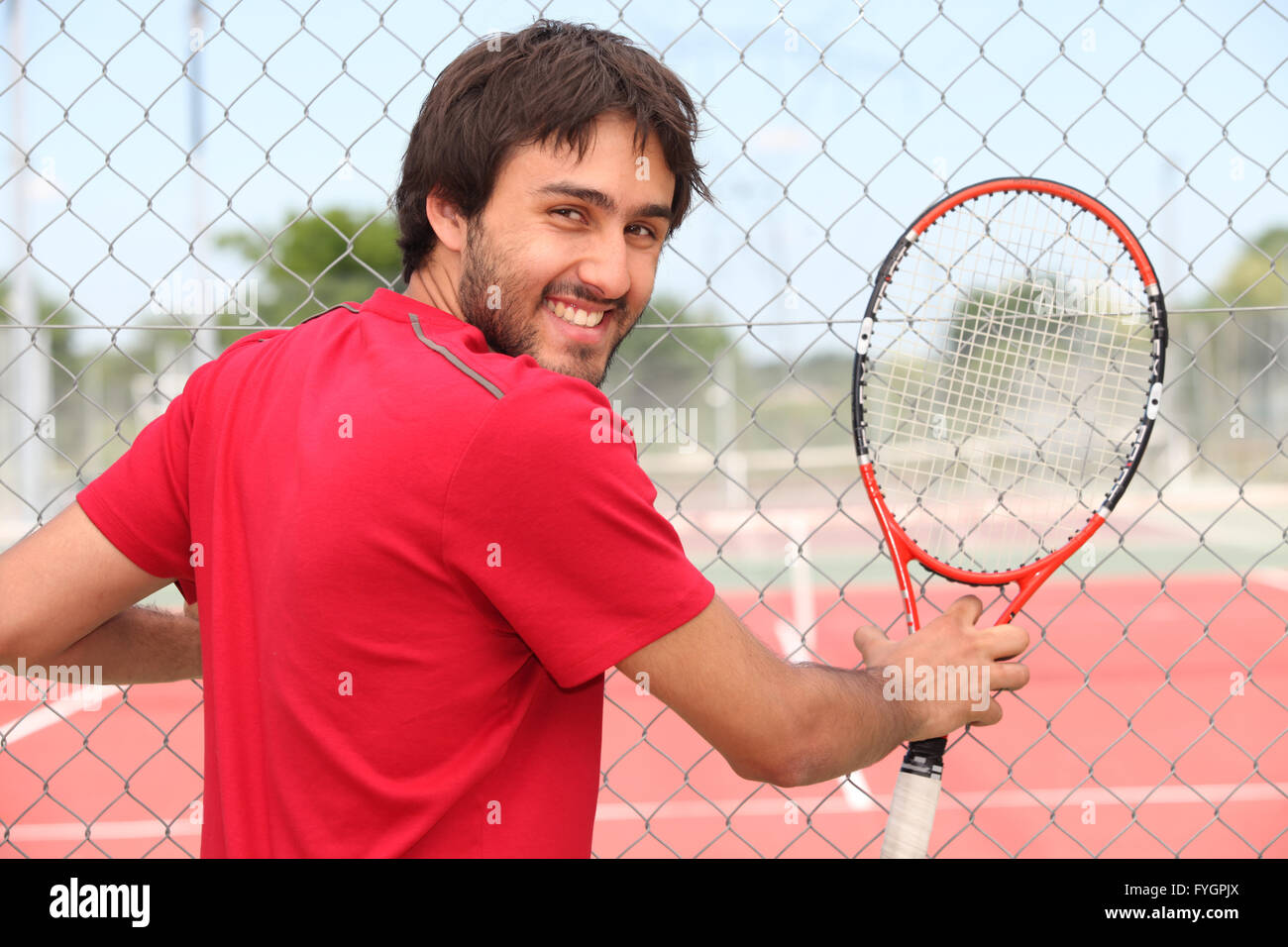 Lächelnder Mann hält Schläger durch Zaun des kommunalen Tennisplatz Stockfoto