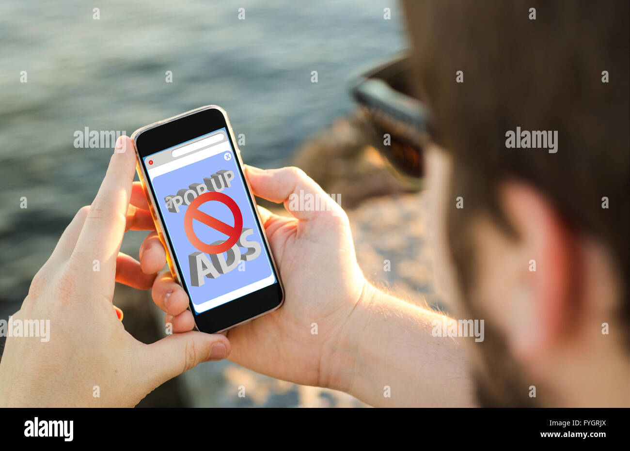 Mann an der Küste mit seinem Smartphone mit Anzeigen-Blocker. Alle Bildschirm-Grafiken bestehen. Stockfoto