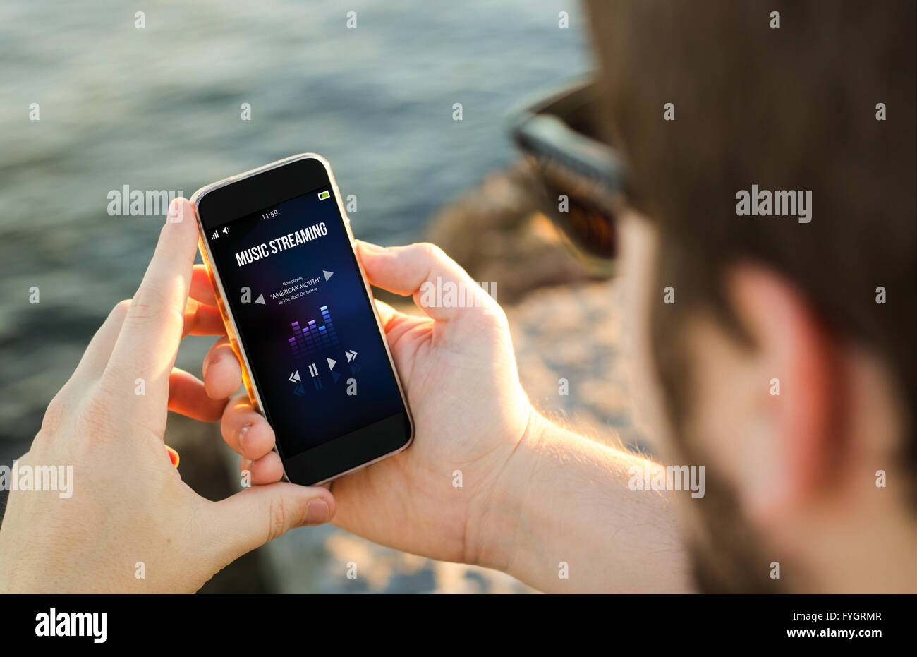 Mann an der Küste mit seinem Smartphone Streamen von Musik zu hören. Alle Bildschirm-Grafiken bestehen. Stockfoto
