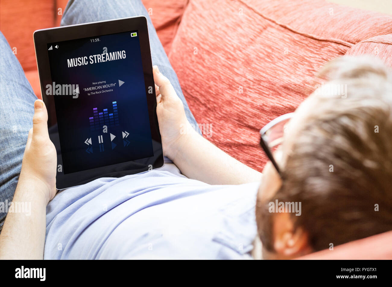 Technologie-Lifestyle-Konzept: Hipster Mann Omusic-streaming auf einem Tablet auf dem Sofa. Alle Bildschirm-Grafiken bestehen. Stockfoto