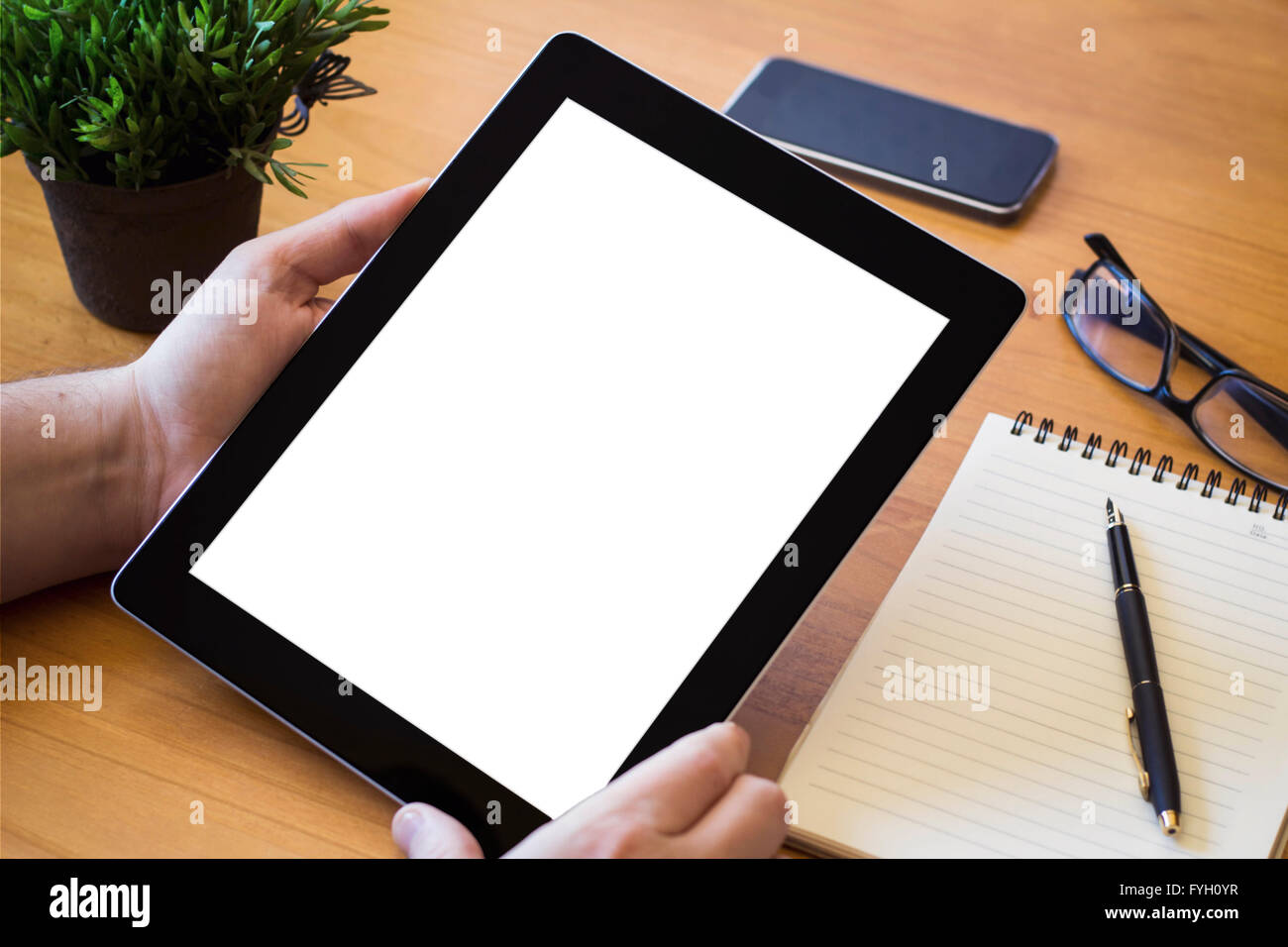Hände eines Mannes hält leere Tablet-Gerät über eine hölzerne Workspace-Tabelle Stockfoto