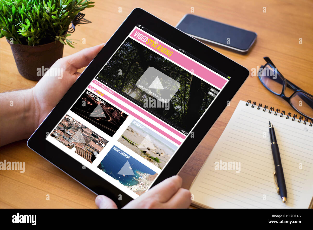 Hände eines Mannes hält einen video-Streaming-Gerät über eine hölzerne Workspace-Tabelle. Alle Bildschirm-Grafiken bestehen. Stockfoto