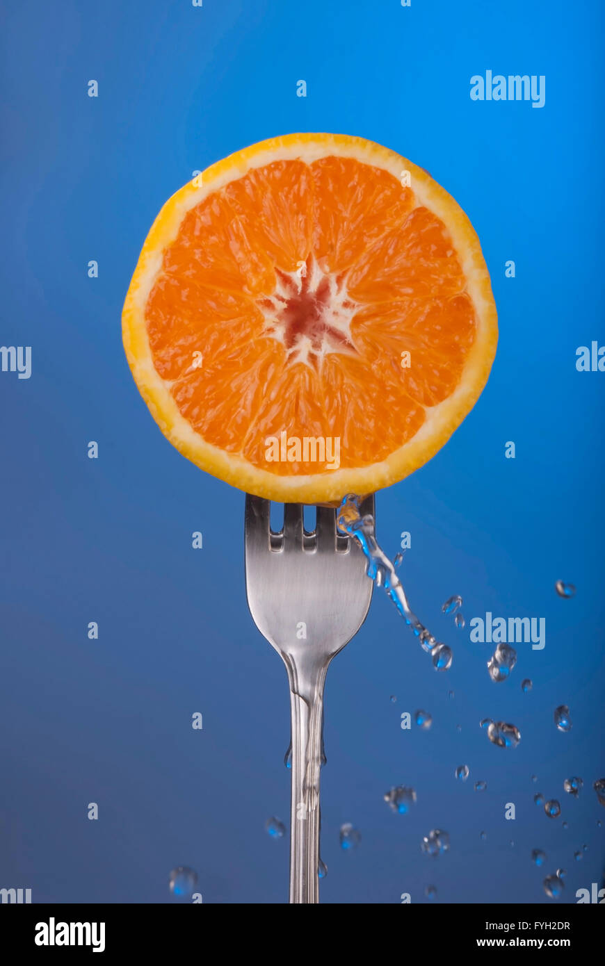 Köstliche orange Frucht halbieren auf Gabel mit Spritzwasser, blaue Farbe Hintergrundfoto Konzept. Stockfoto