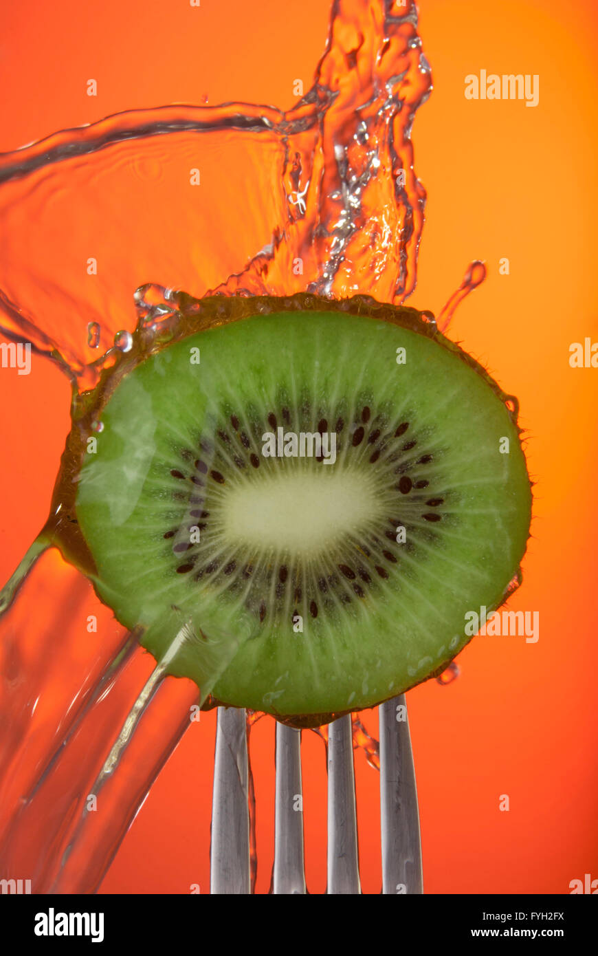 Nahaufnahme von Kiwi-Frucht-Center auf Gabel mit Spritzwasser und farbigem Hintergrund, Konzept Foto. Ideal für die Kampagne "gesunde Ernährung" Stockfoto
