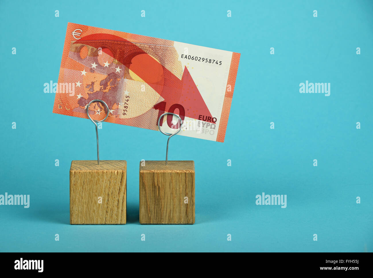 Europäische Wirtschaftskrise, Rückgang der Euro-Währung, zehn-Euro-Banknote mit roten Pfeil nach unten am Holz Metall Halter über blaue backg Stockfoto