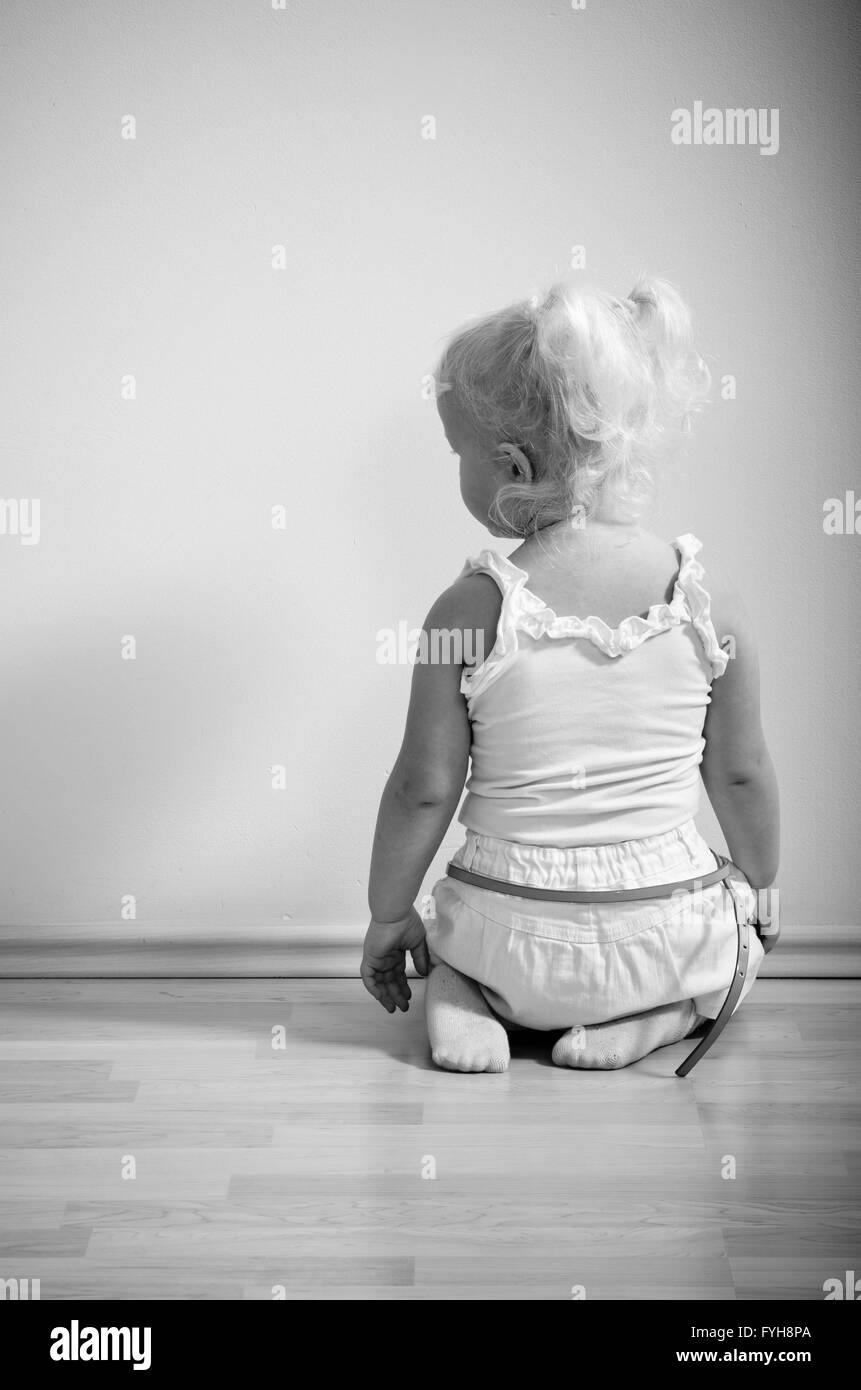 kleines Mädchen sitzt auf den Knien vor der Wand Stockfoto