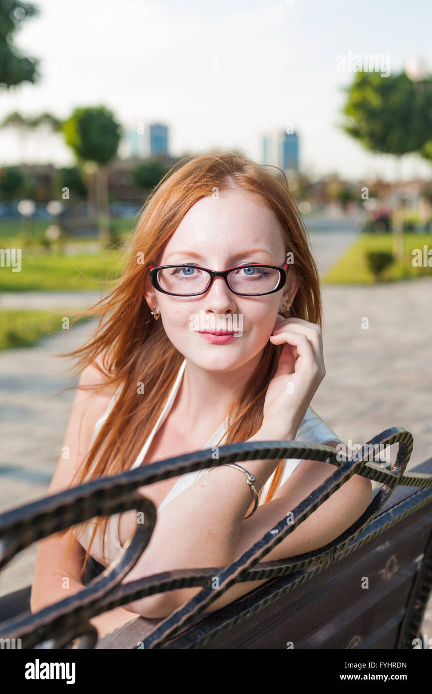 Schöne junge Frau sitzt auf der Bank im Sommerpark Stockfoto