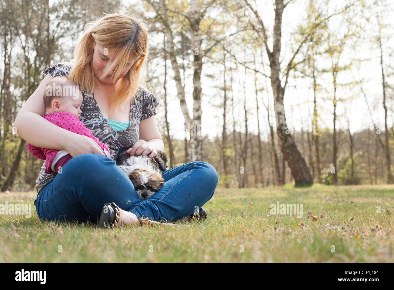 Mutter mit Baby auf dem Rasen und Welpen Stockfoto