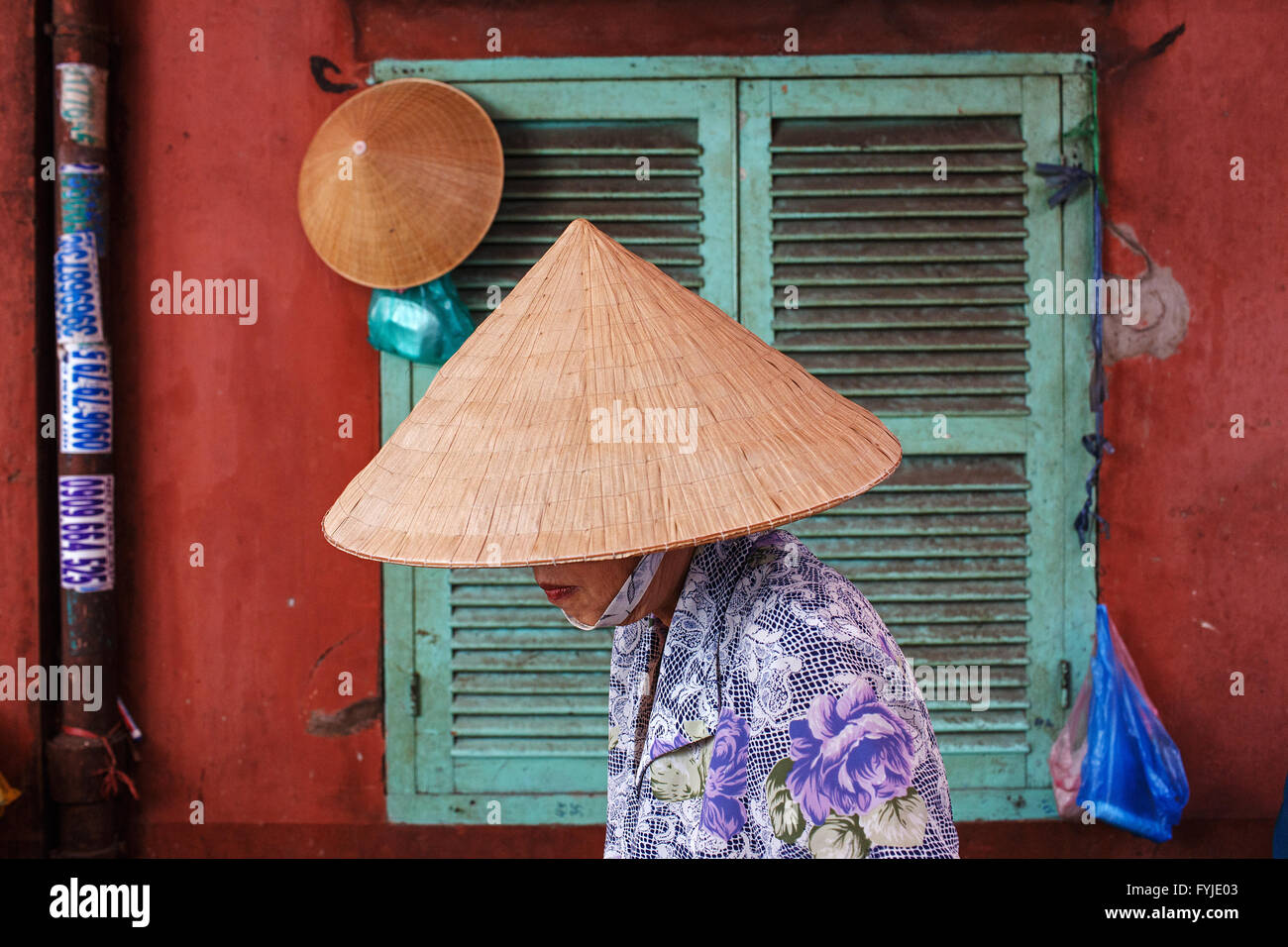 Eine Frau in einem traditionellen vietnamesischen Hut geht von einer roten Mauer in den Gassen von Zentrum von Ho-Chi-Minh-Stadt, Vietnam. Stockfoto