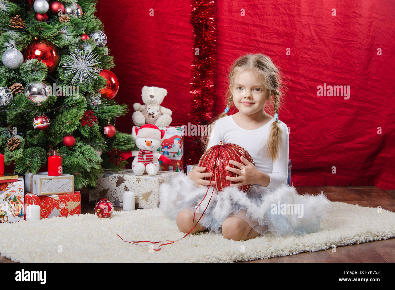 Fünfjähriges Mädchen sitzt mit Weihnachtskugel in einem Baum Stockfoto