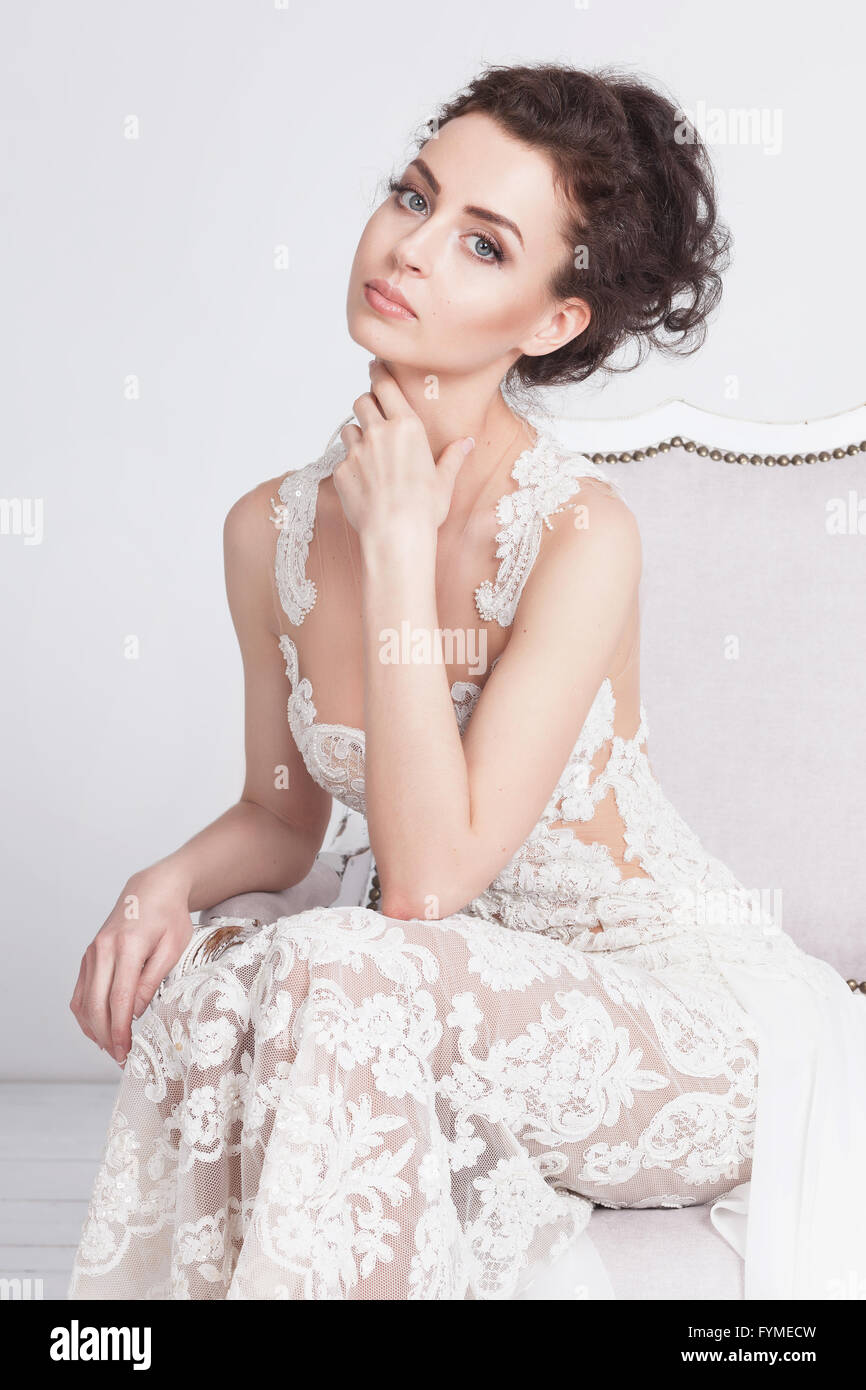 Porträt von schöne junge Braut im Hochzeitskleid edler Spitze. Sie sitzt auf einem weißen Sofa Vintage. Sie ist eine elegante und Sli Stockfoto