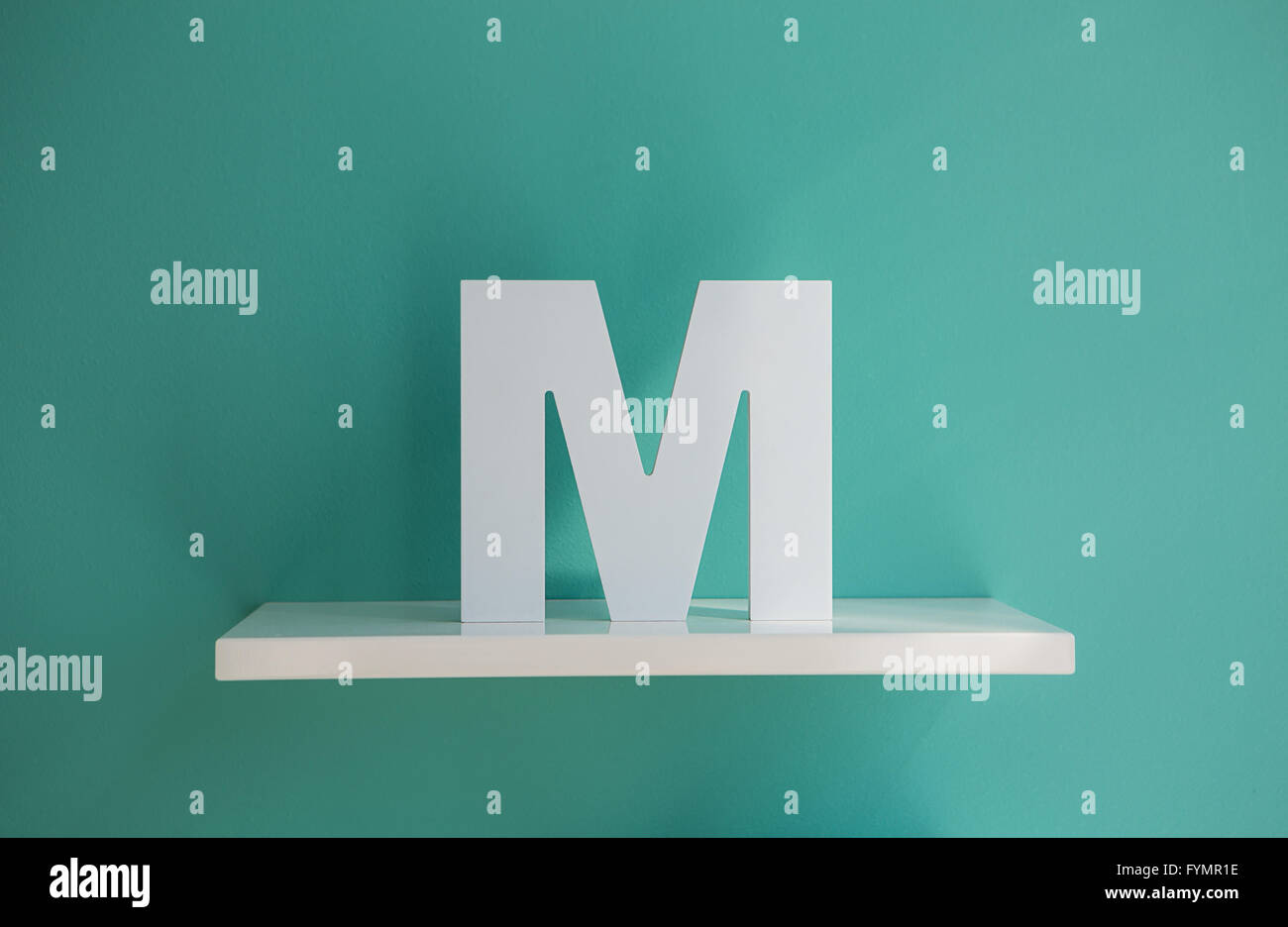 Buchstabe M Türkis Farbe auf einem weißen Regal. Stockfoto