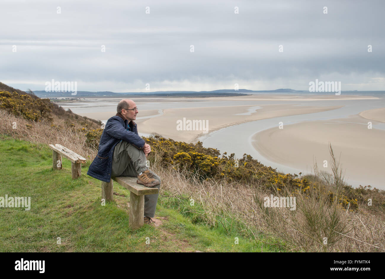 Im mittleren Alter Mann sitzt auf einer Bank, wo Sie über Carmarthen Bay von der Wales Coast Path in der Nähe der Mündung des Flusses Towy Stockfoto Im mittleren Alter Mann sitzt auf einer Bank, wo Sie über Carmarthen Bay von der Wales Coast Path in der Nähe der Mündung des Flusses Towy Stockfoto