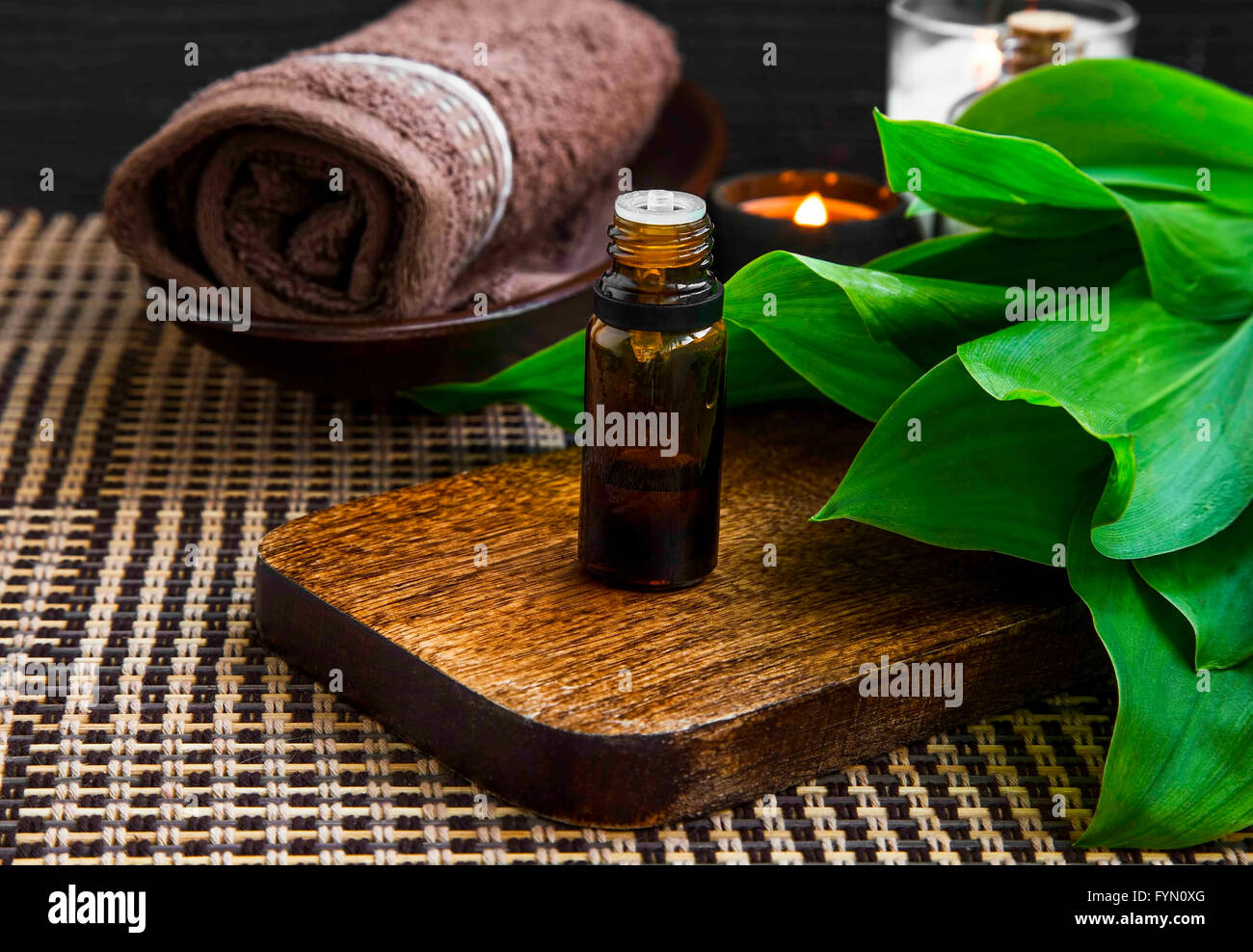 Spa-Ambiente mit Essenz Flasche, Handtuch, Kerze und grüne Blätter für Behandlungen Stockfoto