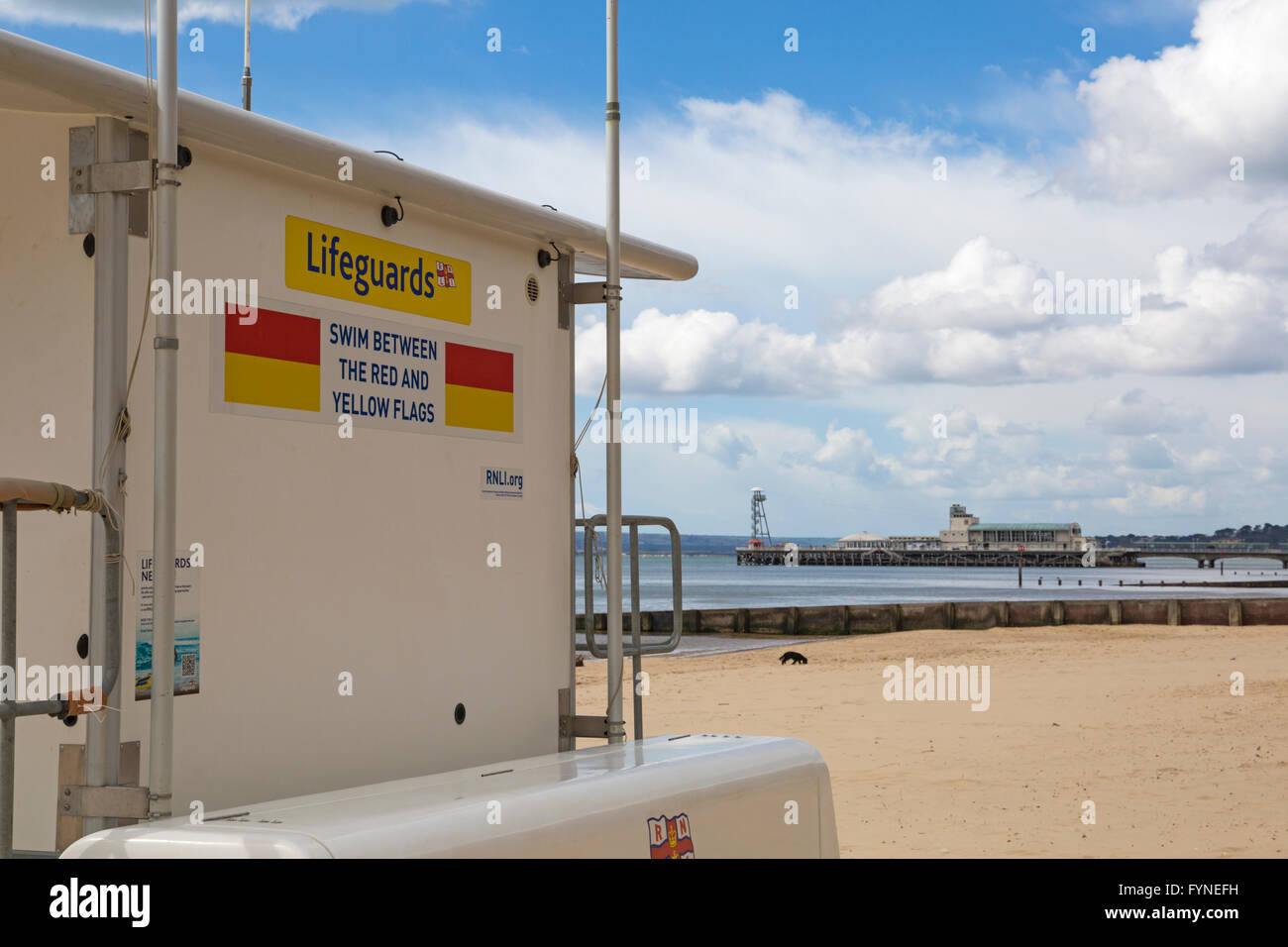 Schwimmen Sie Zeichen auf RNLI Rettungsschwimmer Kiosk am Strand mit Bournemouth Pier in der Ferne zwischen den roten und gelben Flaggen Stockfoto