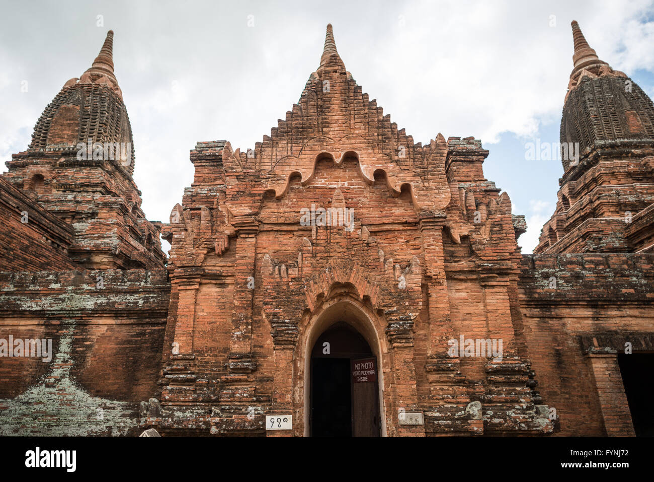 Payathonzu Tempelfassade Bagan Myanmar // BAGAN, Myanmar — die verzierte Fassade eines der drei miteinander verbundenen Tempel, aus denen der Payathonzu Tempelkomplex besteht, zeigt nach Jahrhunderten der Exposition verwitterte rote Backsteingebäude. Das Payathonzu (auch bekannt als Paya-thone-zu), das Ende des 13. Jahrhunderts erbaut wurde, ist das einzige bekannte Beispiel für drei miteinander verbundene Schrein-Strukturen in Bagans archäologischer Zone. Der Komplex wurde vor seiner Fertigstellung aus unbekannten Gründen aufgegeben, die wahrscheinlich mit dem politischen Umbruch des späten 13. Jahrhunderts zusammenhängen. Die Tempel enthalten außergewöhnliche Wandmalereien Th Stockfoto