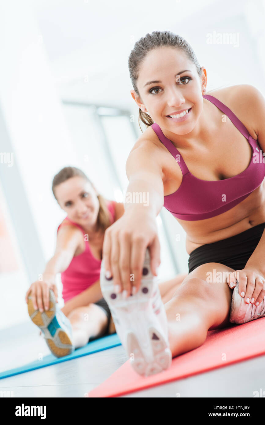 Lächelnde junge Frauen in der Turnhalle eine stretching-Übung für die Beine auf eine Matte, Fitness- und Gesundheitskonzept zu tun Stockfoto