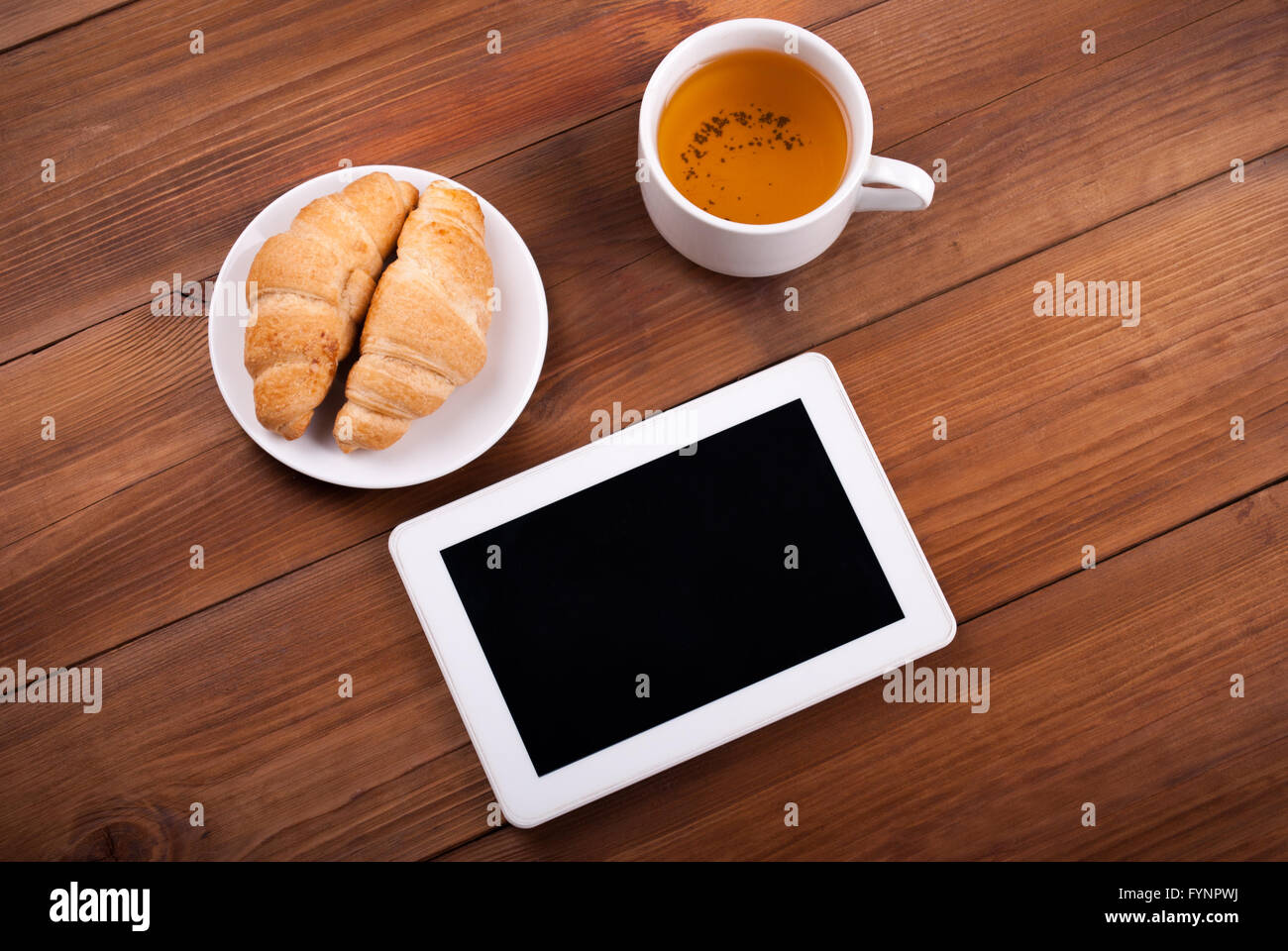 Tasse Tee Tablet Croissants auf einem Holztisch. Stockfoto