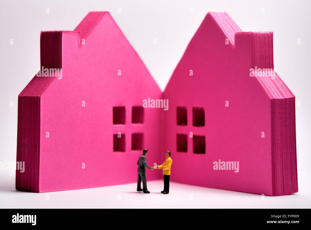 Ein rosa Papierblock in Form von Häusern mit Miniaturfiguren von Geschäftsleuten, die sich die Hände schütteln Stockfoto