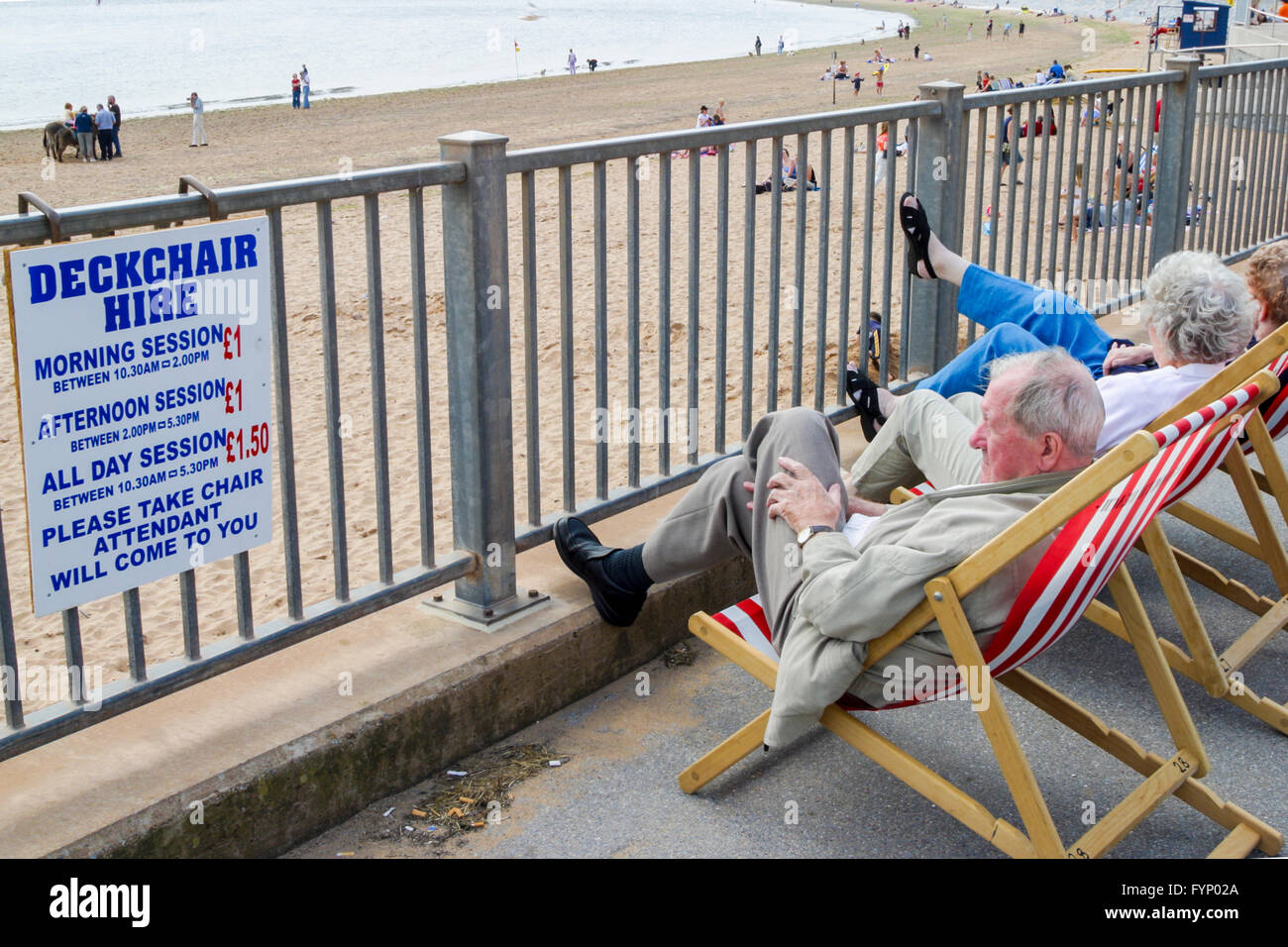 Ältere Menschen sitzen am Strand auf Dechchairs in Exmouth, Devon, England. Stockfoto