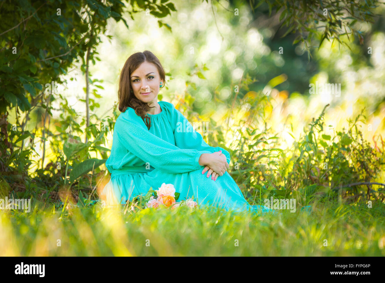Ein Mädchen in einem langen Kleid sitzen auf dem Rasen im Wald bei sonnigem Wetter Stockfoto