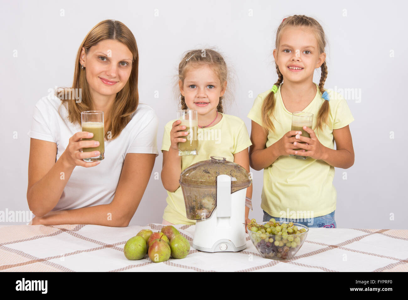 Mutter und zwei Töchter mit Gläsern gemacht frisch Saft von Birnen und Trauben Stockfoto