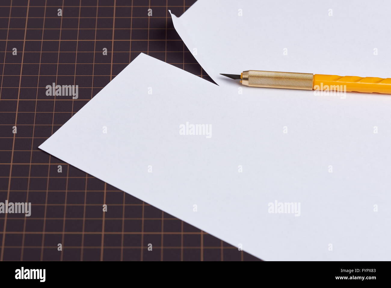 Ein weißes Blatt Papier, das auf eine Schneideunterlage mit einem Messer mit einem gelben Griff oben drauf sitzen geschnitten worden ist. Stockfoto