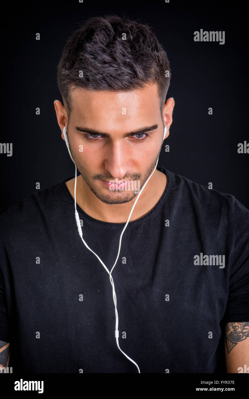 Attraktiver junger Mann mit Kopfhörern Musik hören, blickte auf dunklem Hintergrund Stockfoto