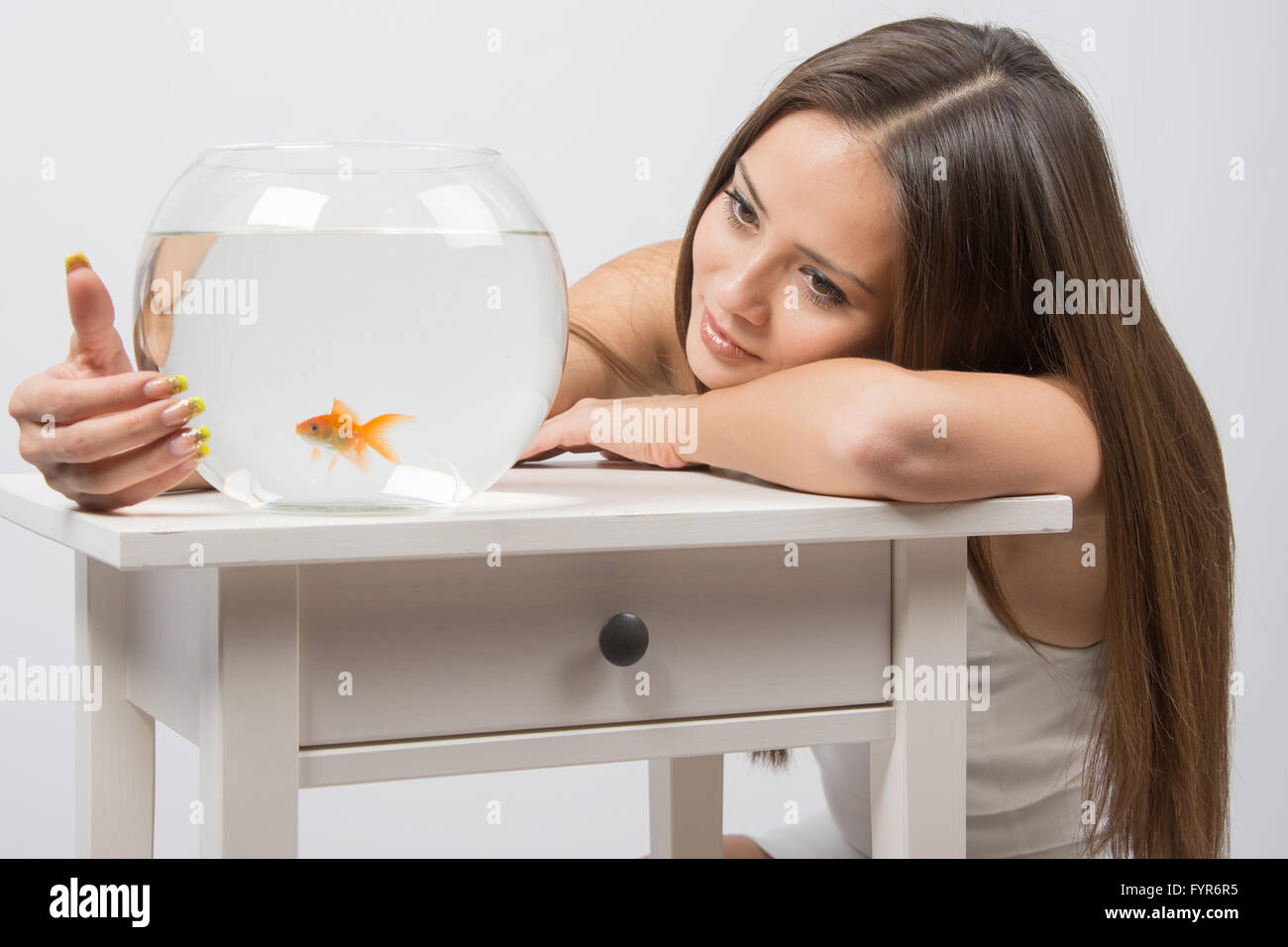 Das Mädchen schaut auf eine kleine Goldfische in einem Goldfischglas Stockfoto