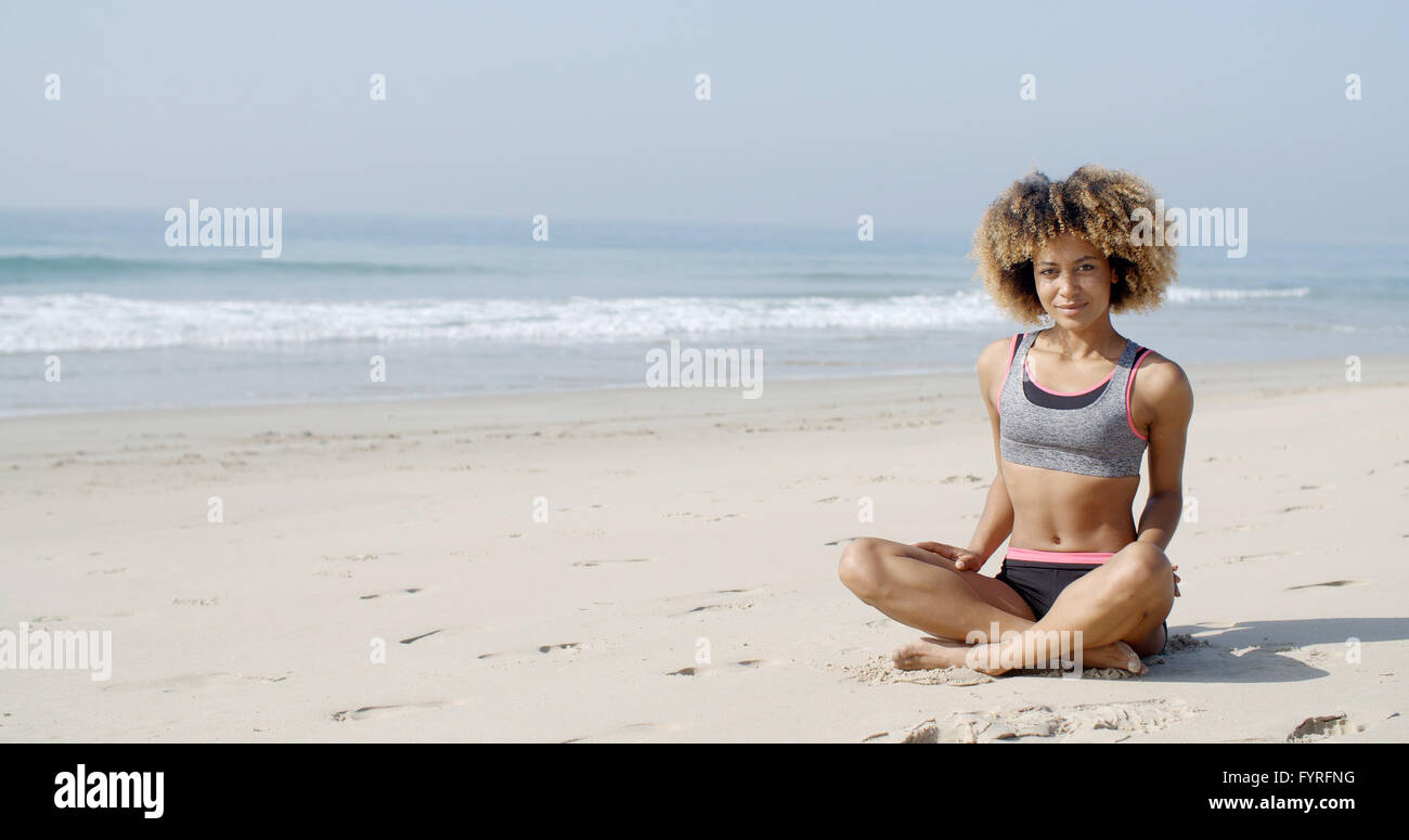 Frau sitzt am Strand In Lotus Pose Stockfoto