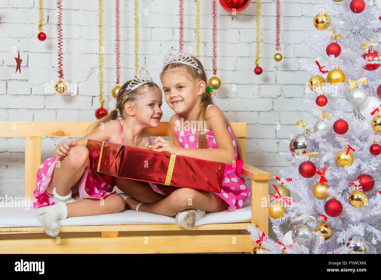 Mädchen flüstert ein Geheimnis, dass einige andere Mädchen sitzen auf einer Bank mit einem Weihnachtsgeschenk Stockfoto