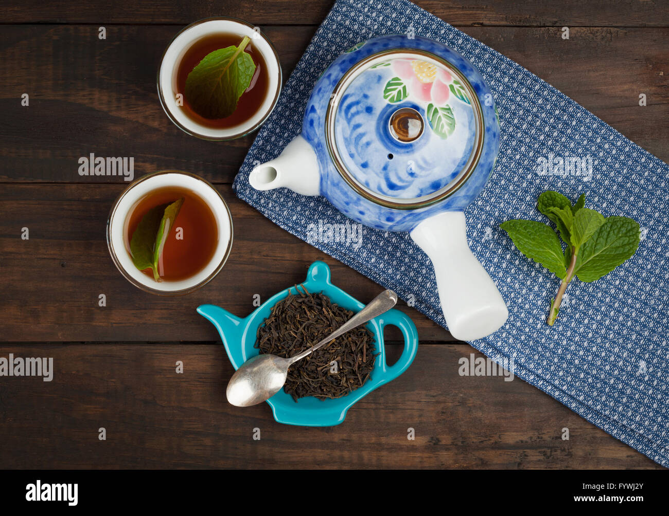 Ganze Blatt-Tee mit Teekanne und zwei Tassen auf Handtuch und hölzernen Hintergrund. Ansicht von oben. Stockfoto