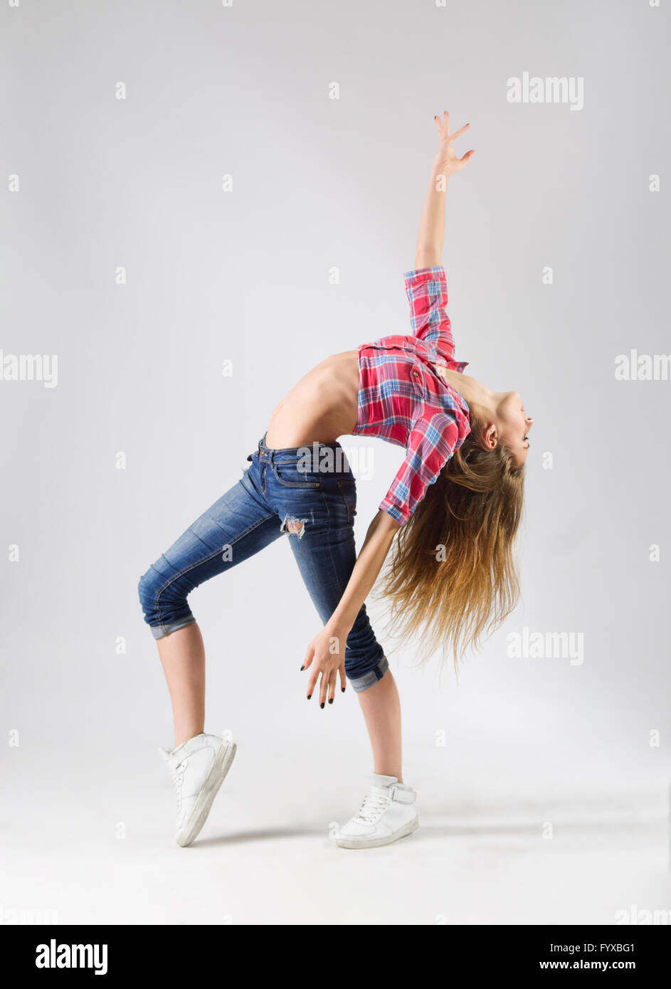 Junge moderne tanzende Mädchen in Jeans auf grau Stockfoto