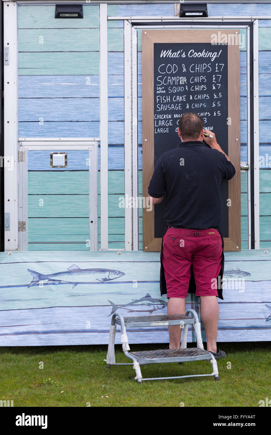 Mann schreibt im April Essensoptionen auf der Tafel im Van Fish & Chips von Bennett auf dem St Georges Day Festival in Poole, Dorset, Großbritannien Stockfoto