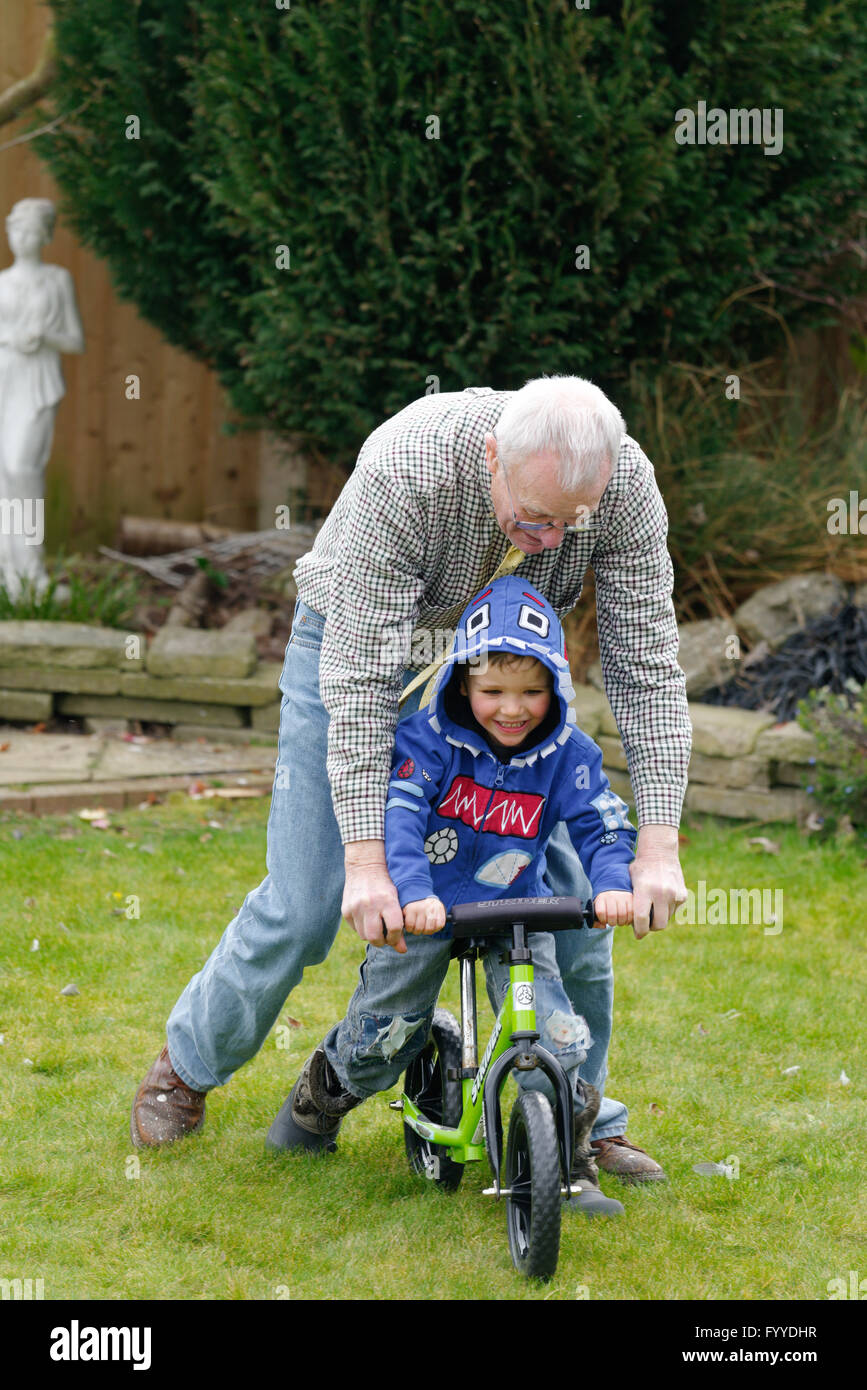 Ein Großvater helfen, sein Enkel (3 Jahre alt), mit dem Fahrrad fahren lernen Stockfoto