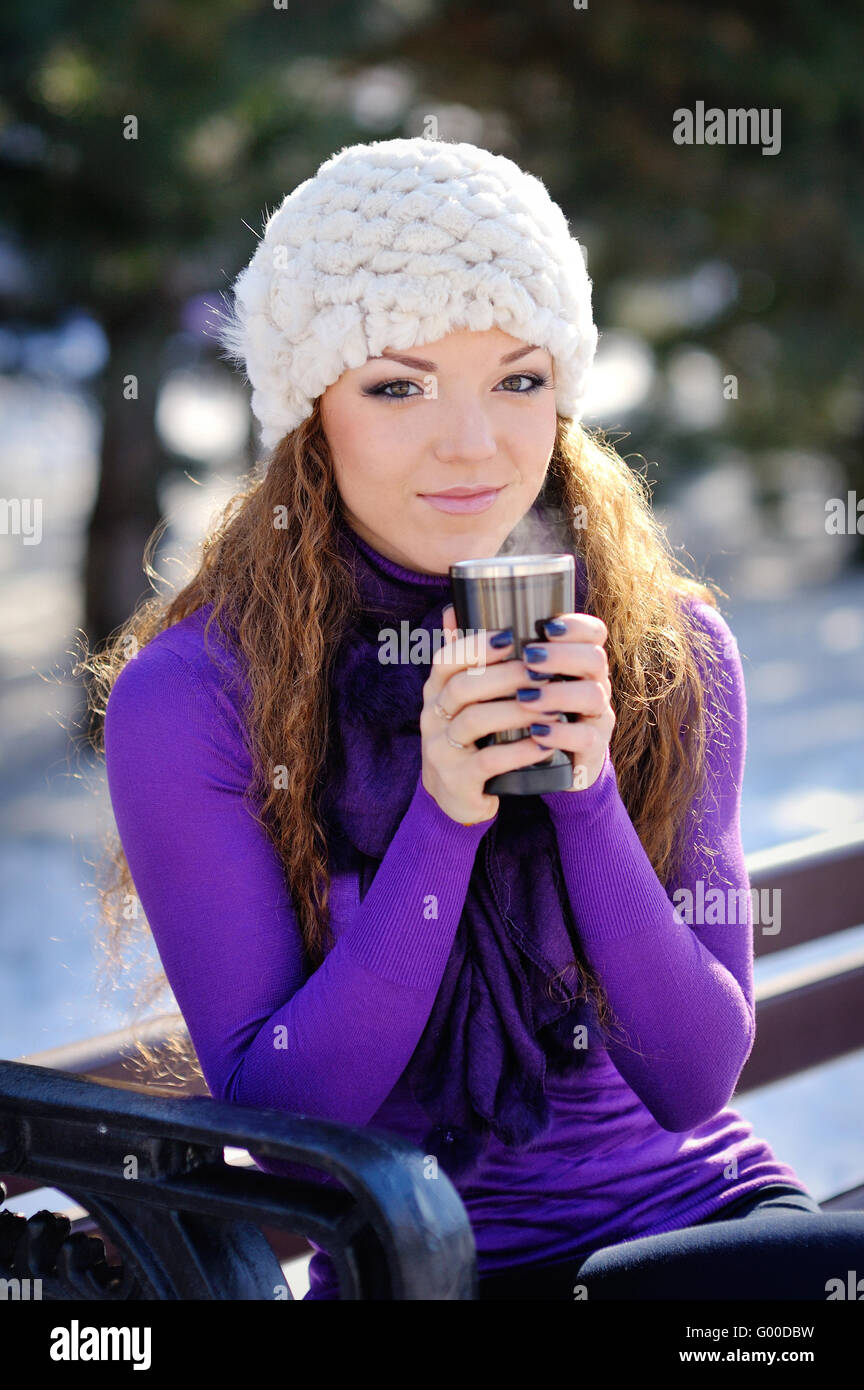 schöne Mädchen sitzen auf einer Bank im Park mit einer Tasse des Winters Stockfoto