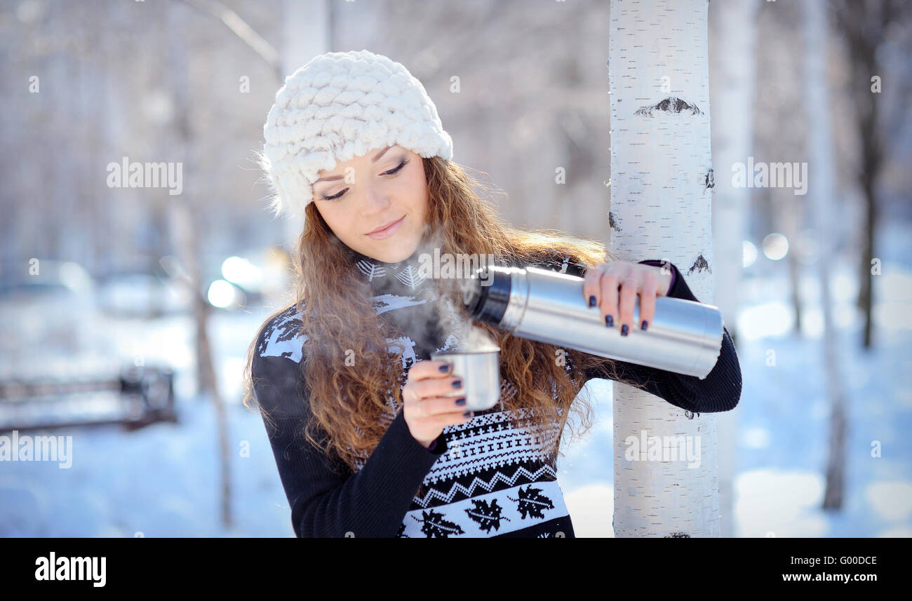 schöne Brünette gießt Kaffee aus einer Thermoskanne für einen Spaziergang im winter Stockfoto