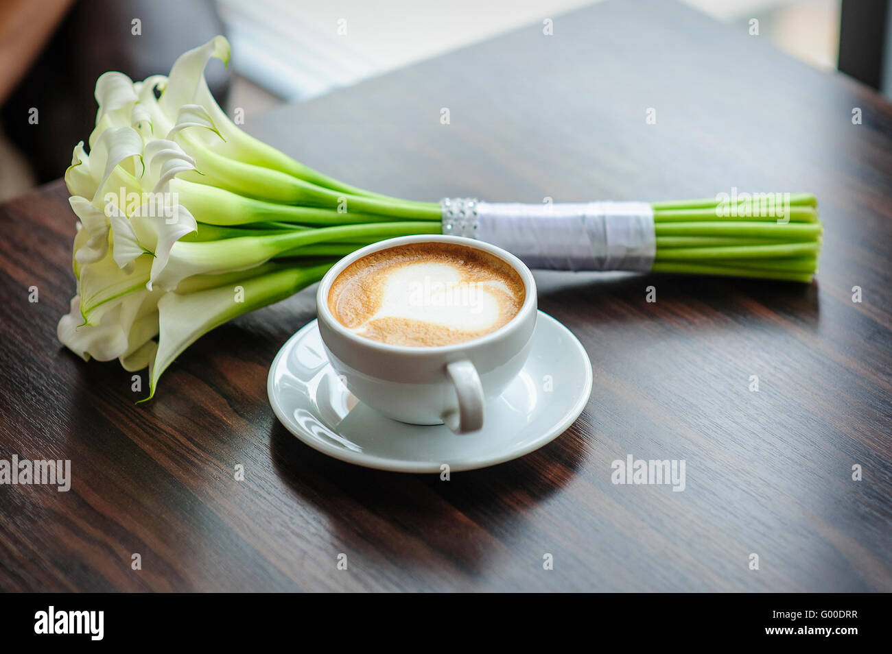 Hochzeit Blumenstrauß Calla Lilien auf einem Tisch mit einer Tasse Kaffee Stockfoto